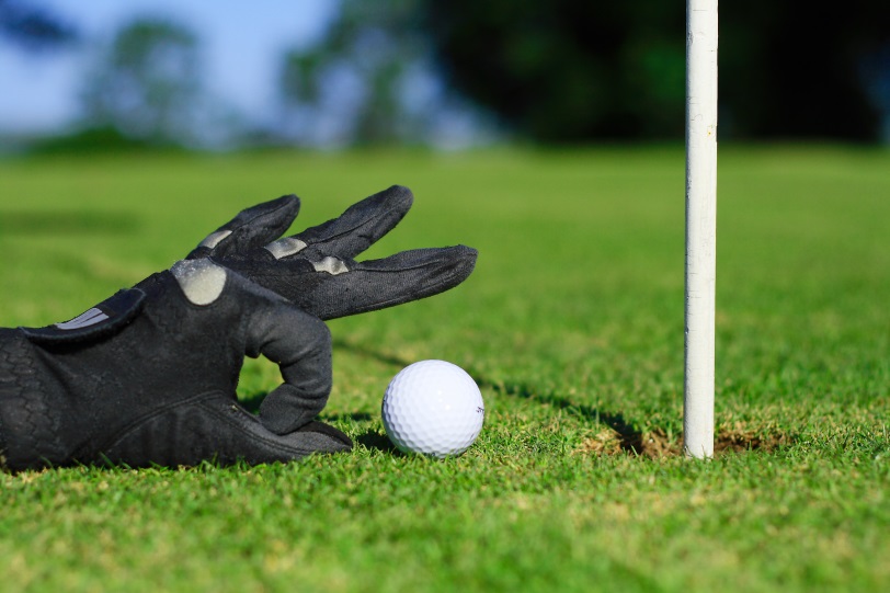 gloved hand flicking a golf ball into the hole